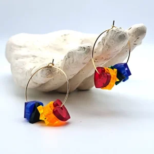 A plaster hand with two hoop earrings hanging from the fingers. The earrings are multi-coloured shapes in the Pride flag colours.