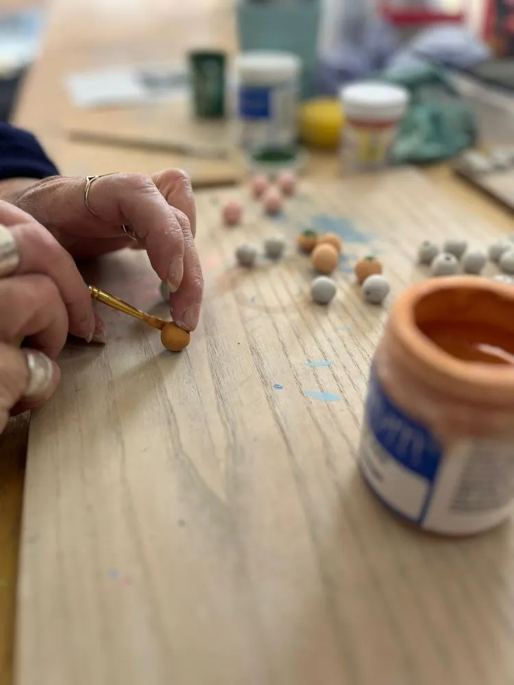 A ceramic bead is being painted with a fine brush.